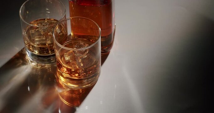 Top-down view of a liquor bottle and two glasses filled with golden brown whiskey and melting ice cubes, Top-down view of two glasses filled with an alcoholic beverage and ice cubes