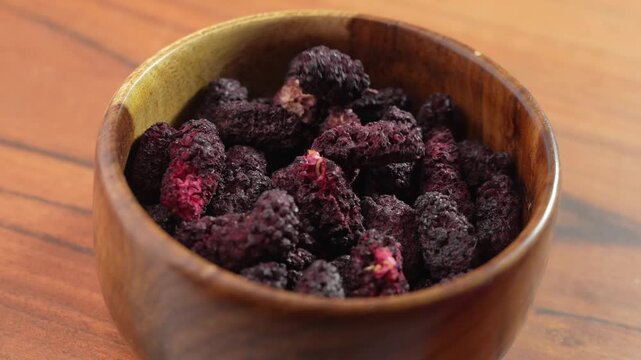 Dried black mulberries on a bowl closeup.
