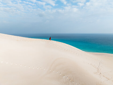Aerial view of pristine white sands meet the turquoise sea, a solitary figure adding a dash of color to the serene landscape, Socotra, Socotra, Yemen.