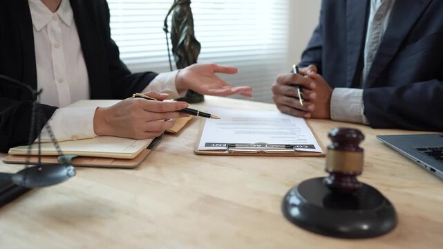 Two lawyers discuss legal documents at a desk, with a scale of justice and gavel symbolizing law, authority, and professional legal consultation in a modern office.