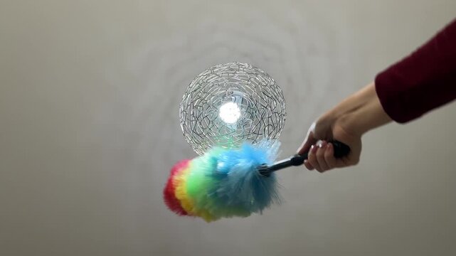 Close up low angle view of woman dusting round silver chandelier with feather duster