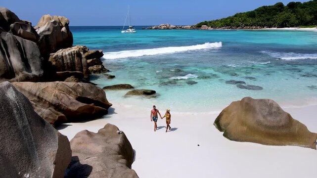 A Couple enjoys a romantic walk along the soft white sands of Anse Cocos beach in La Digue Island, Seychelles. Turquoise waters gently lap against the shore, creating a tranquil atmosphere.