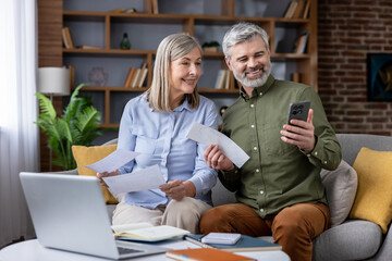 Smiling mature couple managing personal finances and bills together at home, looking at a...
