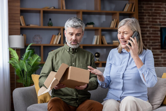 Senior couple on couch arguing with customer service over phone after receiving an empty parcel, frustrated and shocked by an online delivery scam and e-commerce fraud