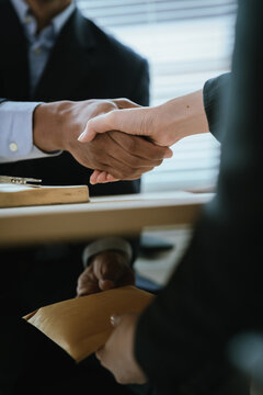 Close-up of hands exchanging a sealed envelope filled with cash under a desk, symbolizing bribery, corruption, illegal transaction, and unethical business practice.