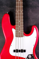 Fototapeta premium Detail of a red electric bass guitar with visible fretboard and headstock on neutral textured background. Music instrument concept, rock and funk sound, studio close up. 