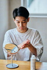Asian young man applying skincare lotion in front of mirror