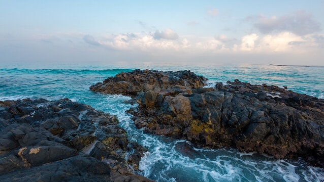 Rocky coastline with turquoise waves under pastel sky