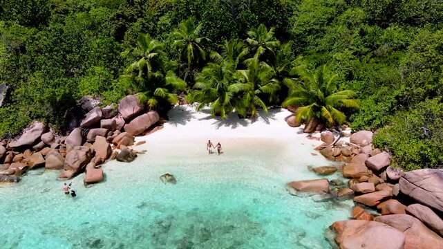 Explore the breathtaking landscapes of Anse Lazio in Praslin, Seychelles. A diverse couple of a man and woman walking on the beach during vacation, drone top view