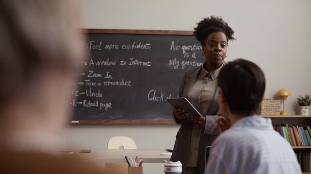 Black female teacher leading interactive classroom discussion with adult students, standing in front of them against chalkboard