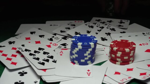 Hand placing poker chips on playing cards during a card game, showcasing a mix of red, blue, and green chips on a green felt table