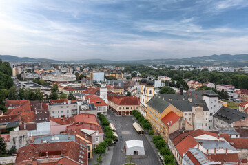 Aerial view of Trenc&iacute;n&rsquo;s Mierov&eacute; Square with City Tower, Piarist Church of St. Francis Xavier and red rooftops framed by modern city and distant hills