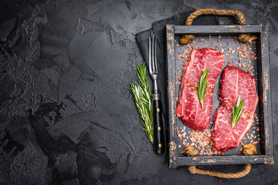 Raw Top blade steak, shoulder beef meat in wooden tray. black background. top view