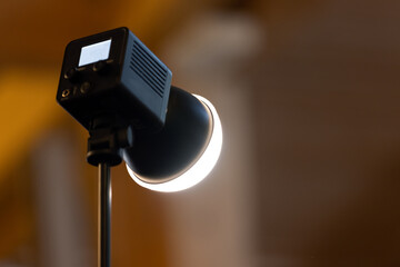 Close-up of a studio lamp spotlight emitting a warm LED glow on an adjustable stand, used for...