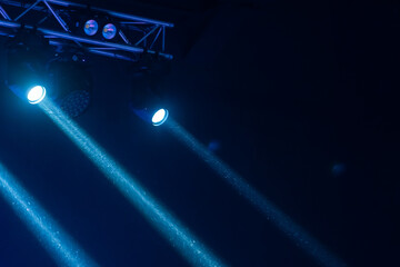 Naklejka premium Blue spotlights cast dramatic beams through haze over a concert stage truss, creating a moody atmosphere for live music, performance and entertainment production