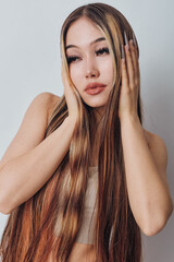 Fototapeta premium Woman with long straight hair and natural makeup posing with hands near face on light background. Beauty, fashion, hairstyle and portrait with soft lighting and casual style.