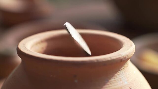 A coin dropping into a clay jar, evoking savings and wealth accumulation, ideal for financial growth themes or advertisements.