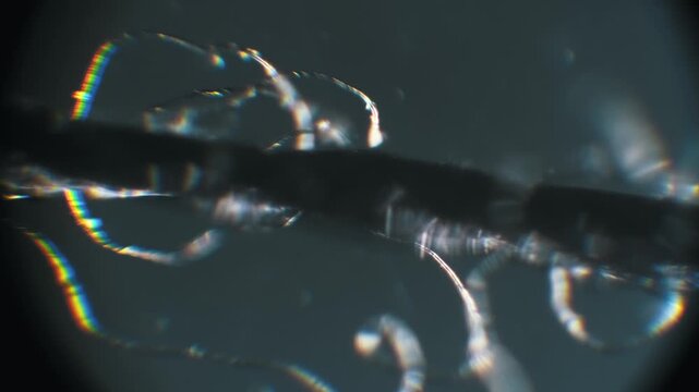 Extreme close-up of individual thread filaments using dark field microscopy. Spectral colors and rainbow reflections create an abstract pattern with moving focus.