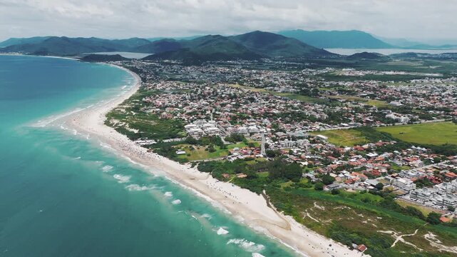 Aerial view of the sandy beach with people relaxing along the coastline. Campeche beach, Florianopolis, Brazil.