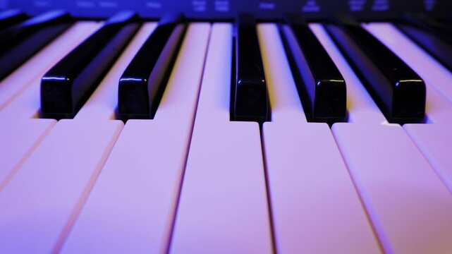 Electronic piano keyboard keys are shown in a close-up, low-angle view. Multicolored club-style lights cycle through pink, blue, and green, creating a vibrant and dynamic mood.