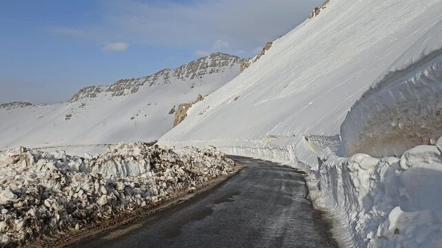 snowy mountain road winding through a bright winter landscape, dark asphalt contrasting with white snowbanks, rocky cliffs, and clear blue sky.  
📍Hawraman Takht, Kurdistan 