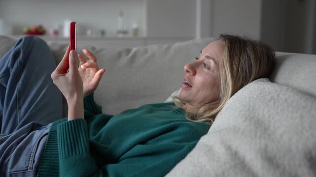 Relaxed woman with phone lying on sofa surfing online web, procrastination at home. Lazy female with social media addiction on smartphone scrolling internet, enjoy virtual life looking at screen. 