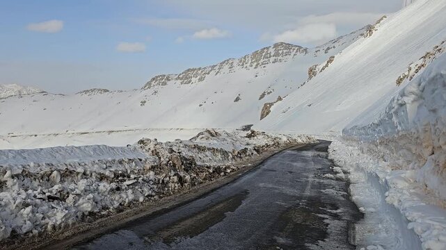 snowy mountain road winding through a bright winter landscape, dark asphalt contrasting with white snowbanks, rocky cliffs, and clear blue sky.  
📍Hawraman Takht, Kurdistan 