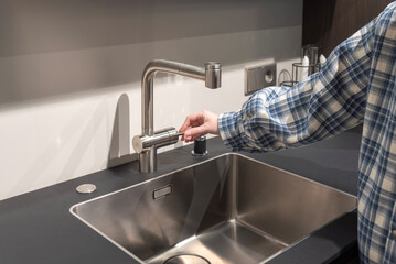 Woman hand on stainless steel kitchen faucet over modern sink