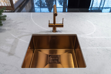 Brushed brass kitchen faucet and sink integrated into marble surface