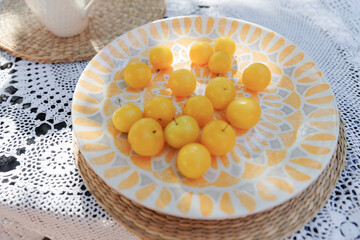 Fresh ripe yellow plums on patterned ceramic plate over woven placemat and crochet lace