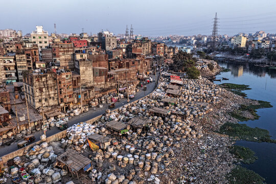 Dhaka, Bangladesh - 05 February 2026: Aerial view of a densely packed urban landscape meeting the riverbank, burdened by heaps of what appears to be waste, juxtaposed against the skyline.