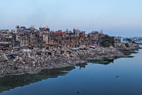 Dhaka, Bangladesh - 05 February 2026: Aerial view of a densely packed urban landscape where buildings meet a riverbank strewn with waste, reflecting the somber hues of the sky.