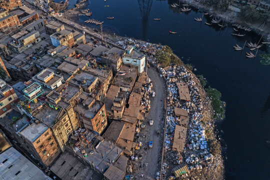 Dhaka, Bangladesh - 05 February 2026: Aerial view of a stark contrast where dwellings meet the waters edge amidst scattered boats and refuse, portraying urban density and environmental challenges..