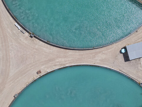 Aerial view of shimmering turquoise water fills circular ponds surrounded by arid land, creating a striking contrast of color and texture, Buckeye, Arizona, United States.