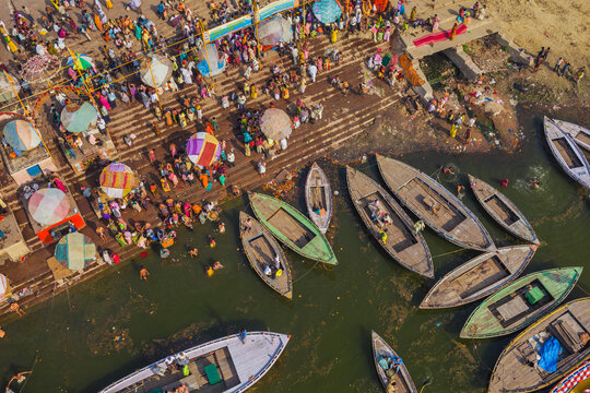 Aerial view of vibrant crowds gather along the ghats, with colorful umbrellas dotting the scene as boats line the riverbanks, Varanasi, Uttar Pradesh, India.