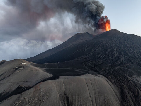 Aerial view of Mount Etna erupts, spewing fiery lava and billowing smoke against the twilight sky, a stark contrast of destruction and beauty, Catania, Sicily, Italy.