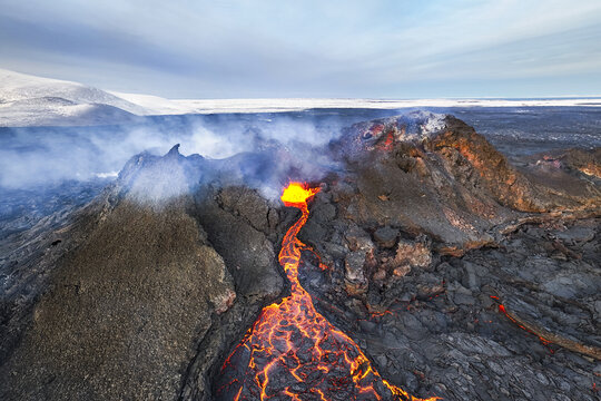 Aerial view of molten lava flows like fiery rivers from the volcanic eruption, contrasting against the stark, snow-covered landscape, Grindavikurbaer, Iceland.