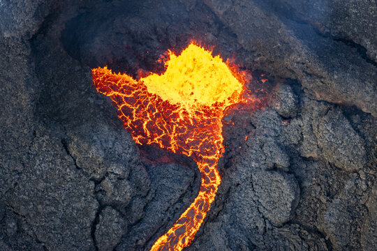 Aerial view of fiery molten lava flows contrasting with the dark, rugged landscape of the Reykjanes Peninsula, Grindavikurbaer, Iceland.