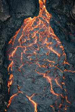 Aerial view of molten lava cascading down dark volcanic rock, a fiery river against a stark, contrasting landscape, Grindavikurbaer, Iceland.