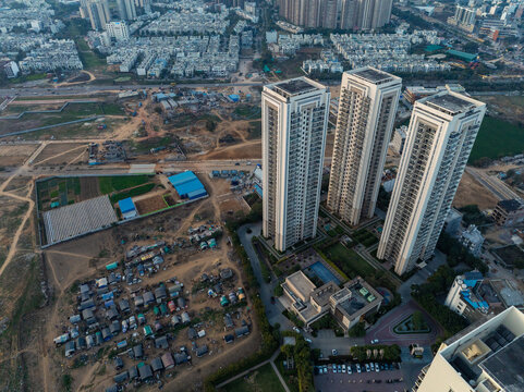 Aerial view of stark contrasts between modern high-rises and sprawling settlements under a hazy sky, showcasing urban stratification, Gurugram, Haryana, India.