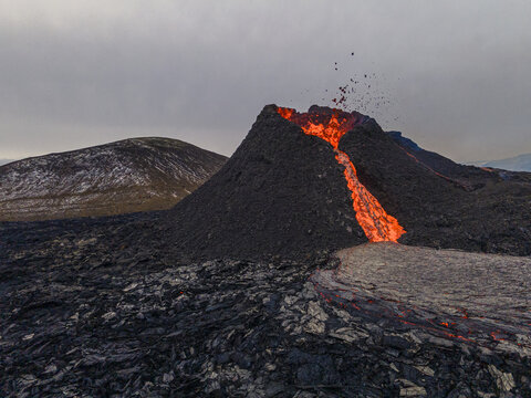 Aerial view of molten lava flowing down the dark volcanic cone, contrasting sharply with the surrounding rugged landscape, Grindavik, Grindavikurbaer, Iceland.