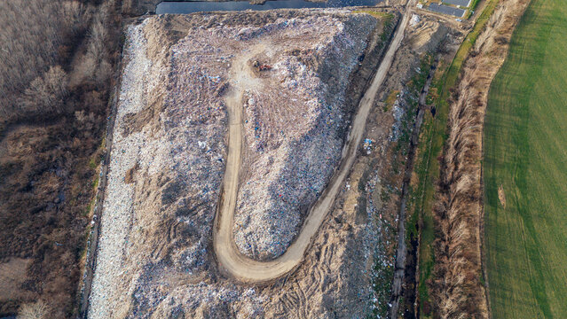 Aerial view of a vast landfill site sprawling beside a field, the stark contrast of waste against the green, Sremska Mitrovica, Vojvodina, Serbia.