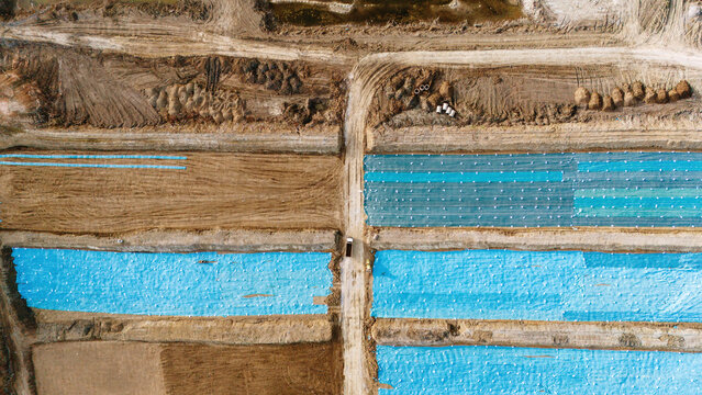 Aerial view of vibrant blue plastic sheeting contrasts against the earthy tones of ploughed fields, creating a patchwork of color and texture, Sremska Mitrovica, Vojvodina, Serbia.