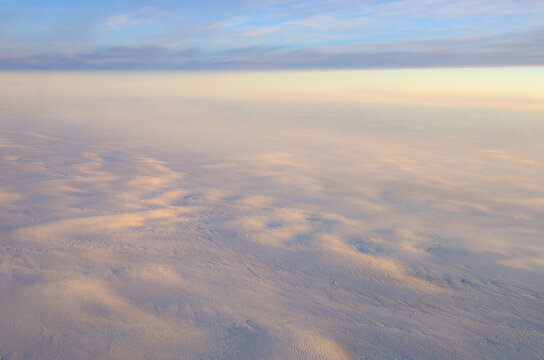 Aerial view of a mesmerizing blanket of clouds, painted with soft hues of pink and blue, stretches as far as the eye can see, Greenland.