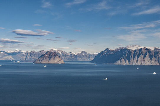 Aerial view of deep blue waters speckled with icy white fragments contrasting with the rugged, snow-dusted mountains, Nuuk, Greenland.