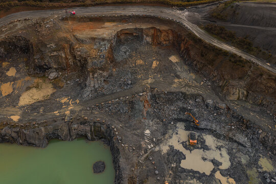 Aerial view of a rugged quarry's edge where the raw earth meets the reflective waters, punctuated by the machinery's presence, Peumerit, Brittany, France.