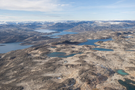 Aerial view of a rugged landscape dotted with sapphire lakes mirroring the sky, contrasted against the earthy tones of the terrain, Nuuk, Greenland.