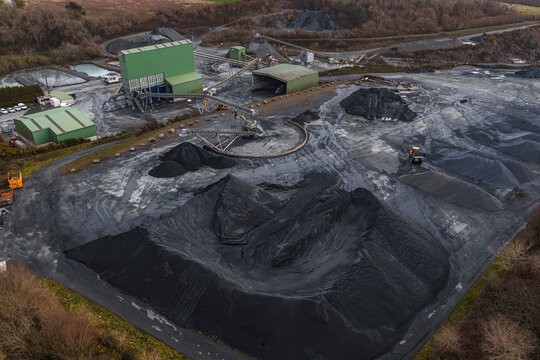 Aerial view of dark, imposing mounds of raw material contrast with the industrial buildings, creating a stark landscape, Peumerit, Brittany, France.