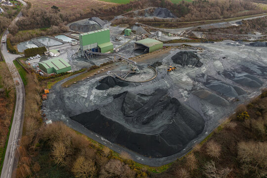 Aerial view of the stark, grey quarry contrasting sharply with the surrounding green trees and industrial buildings, Peumerit, Brittany, France.