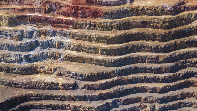 Aerial view of terraced earth carved in layers, revealing a palette of ochre, rust, and grey, creating an abstract landscape of industrial artistry, Rio Tinto, Andalusia, Spain.